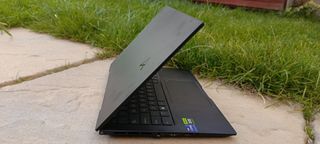 A black ASUS Zenbook Pro 14 OLED sitting on a patio in front of a grassy lawn