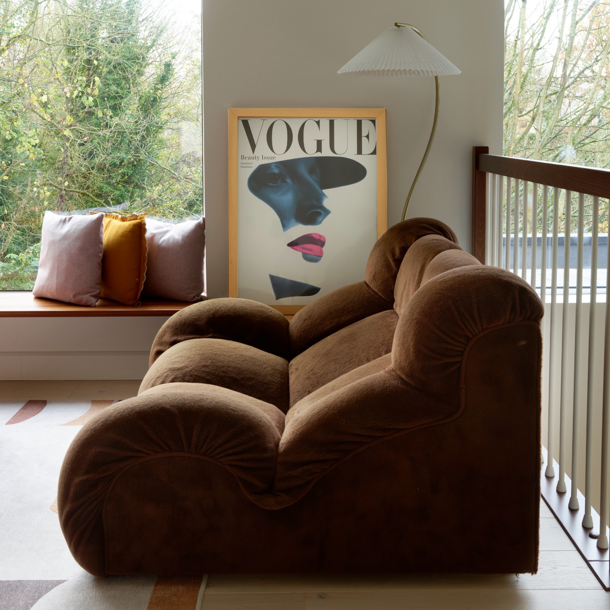 A living room with a modern, low-profile brown sofa with a curved floor lamp next to it and a framed Vogue magazine cover