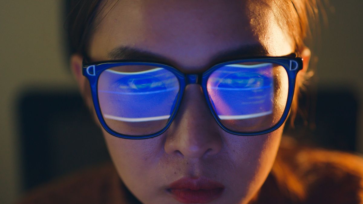 A woman staring at a computer screen with the screen reflected in her glassess