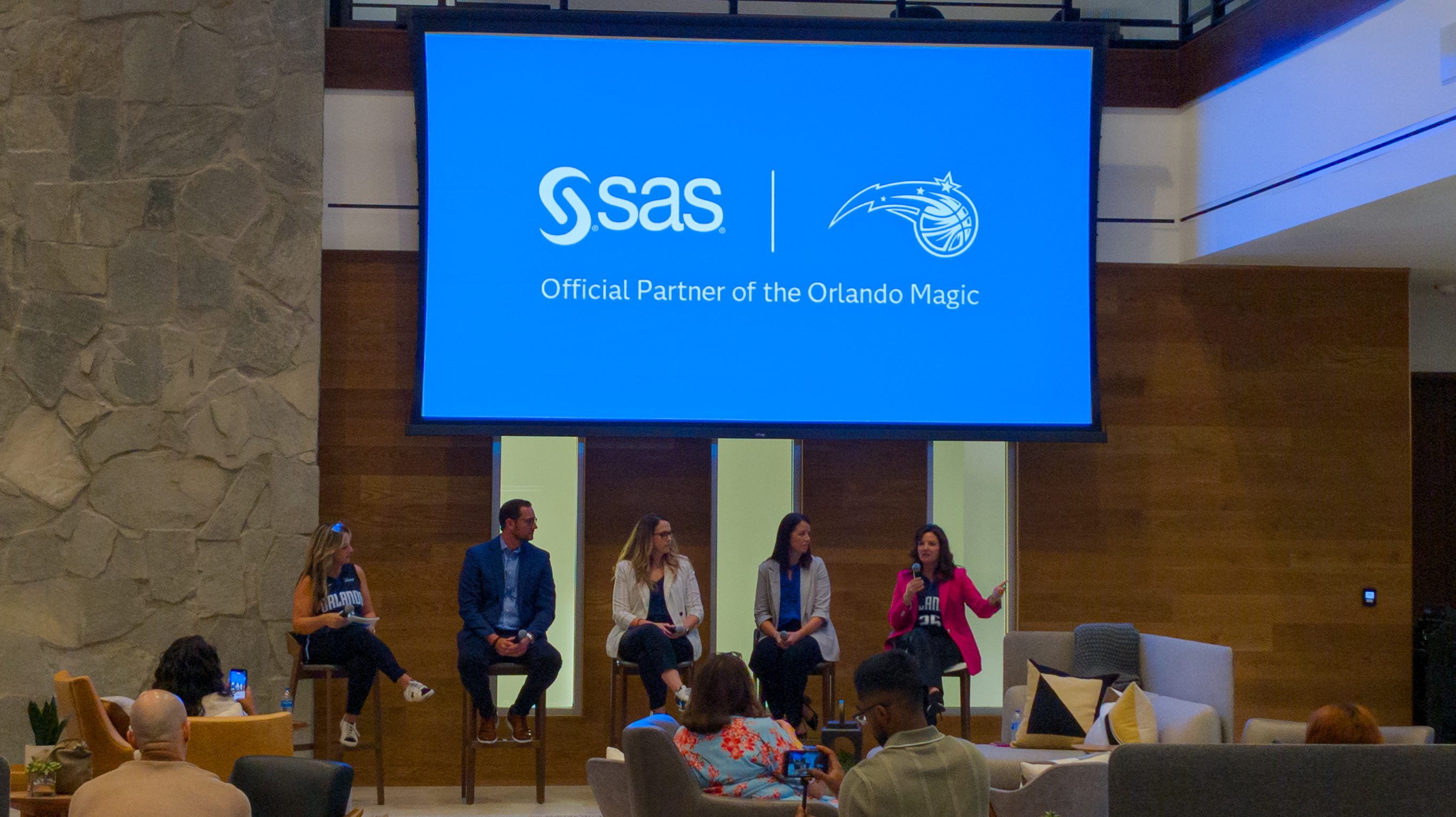 Representatives from the Orlando Magic talking at a SAS Innovate panel. Above them, a screen shows the logos of both SAS and the Orlando Magic, with a caption 'Official Partner of the Orlando Magic'.
