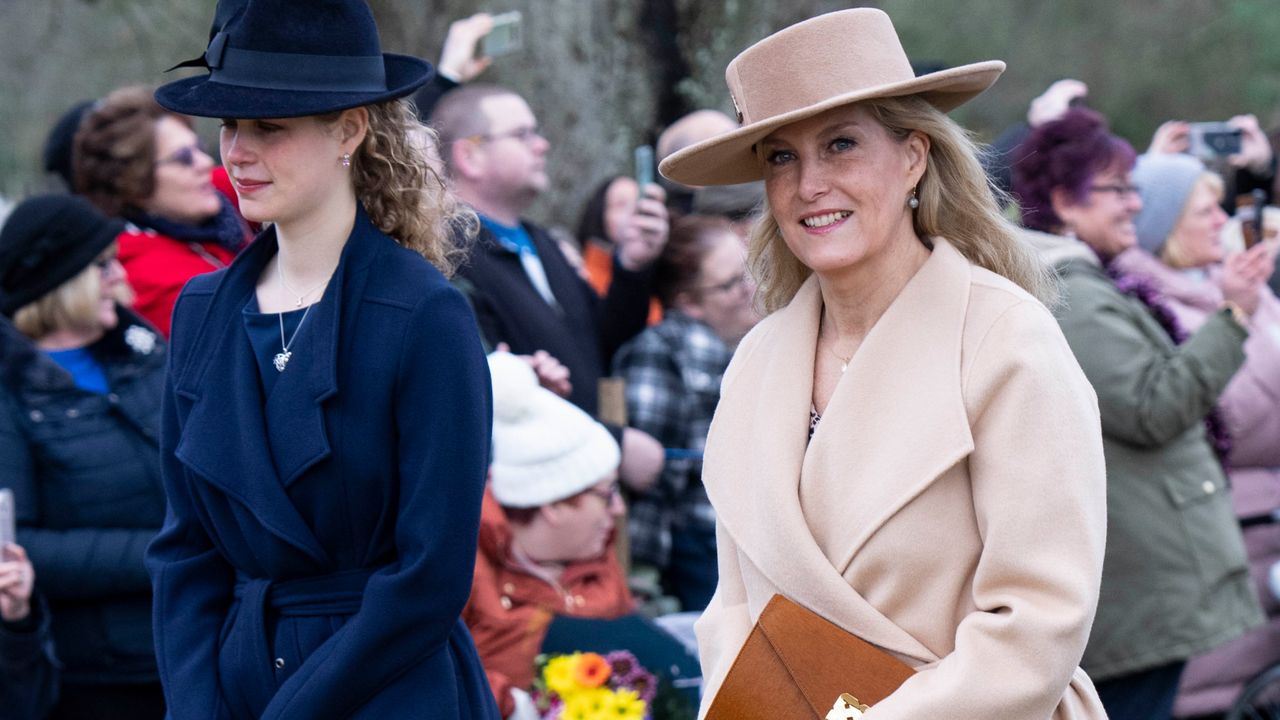 Sophie, the Duchess of Edinburgh wearing a tan coat and hat walking. next to Lady Louise Windsor in a navy coat with crowds of people behind them