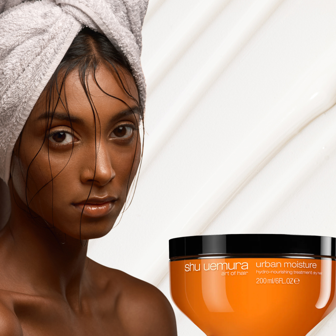 A woman with a towel on her head beside three tubs of hair masks for curly hair. 