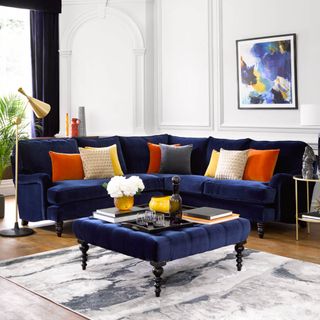 large white living room with blue velvet corner sofa and colourful cushions