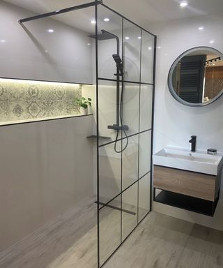 A gray and white bathroom with a walk-in shower, sink, and mirror