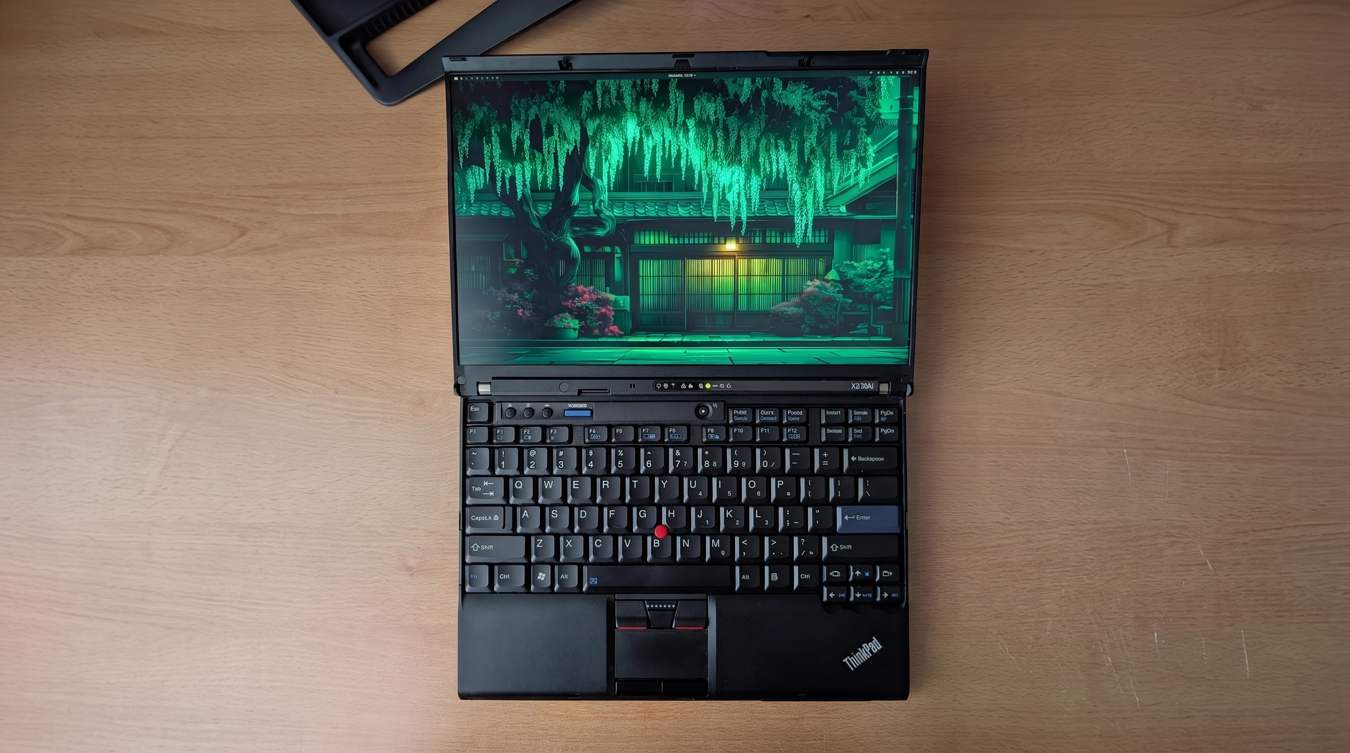 An open Lenovo ThinkPad laptop on a wooden surface, displaying a vibrant digital artwork of a Japanese garden at night, with a focus on lush greenery and traditional architecture.