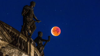 blood red moon during a total lunar eclipse next to a building with two statues on the roof