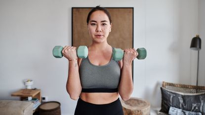 A woman performing a biceps curl with dumbbells during a home workout 