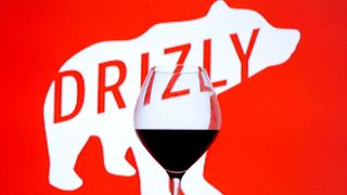 A wine glass against a background of the Drizly logo, the company name emblazoned on the silhouette of a white bear against red