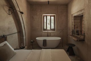 A bedroom with plaster walls, and a tub inside