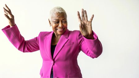 Portrait of beautiful senior woman with short hair wearing bright pink jacket on white background