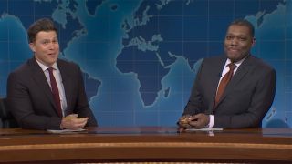 Colin Jost and Michael Che (l to r) make funny faces while wearing suits and ties and sitting at the Weekend Update desk on SNL.