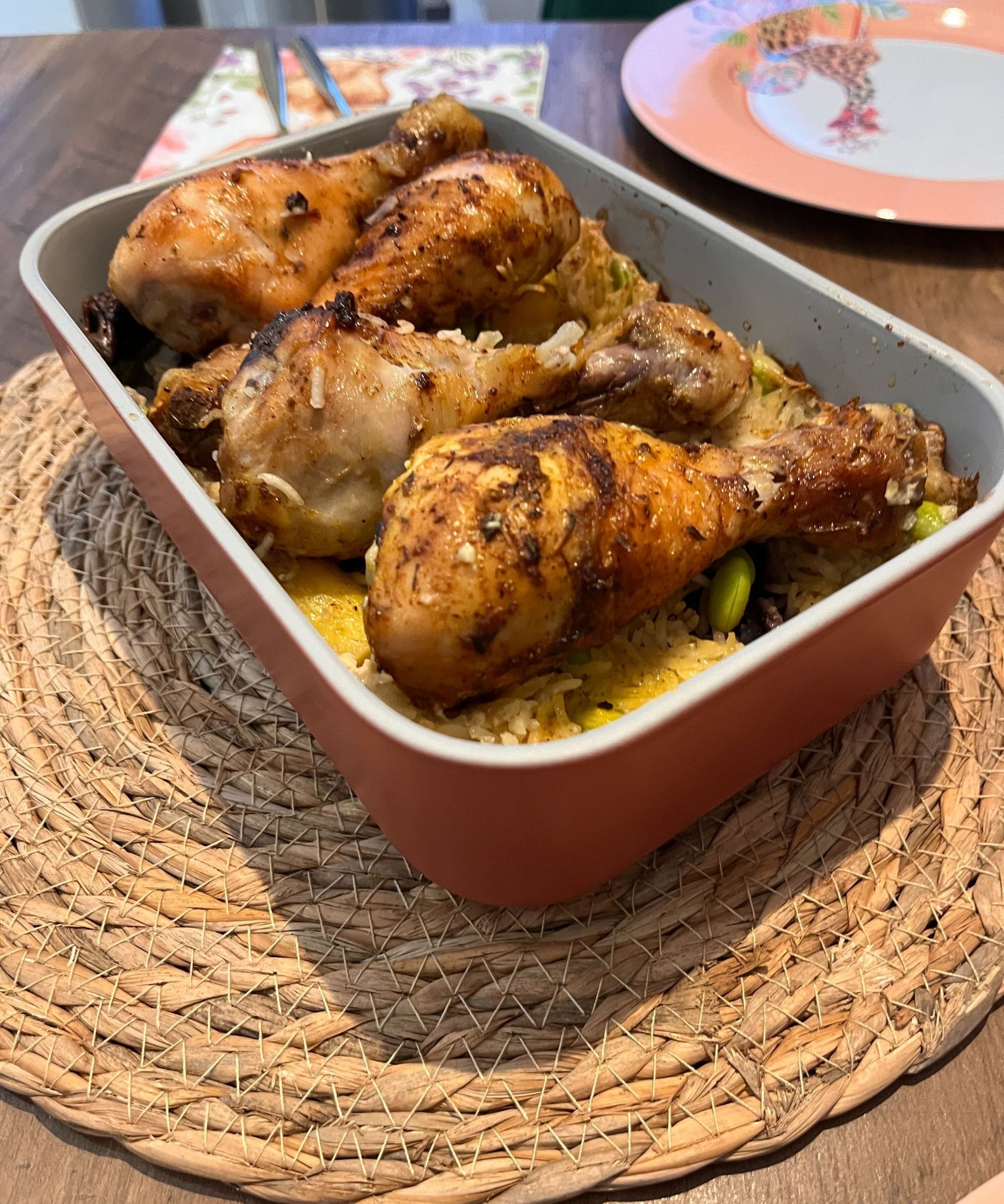 Caraway non toxic food container set in a terracotta color the brand calls Perracotta, shown here filled with oven baked chicken and rice tray bake, on a rattan heat protector