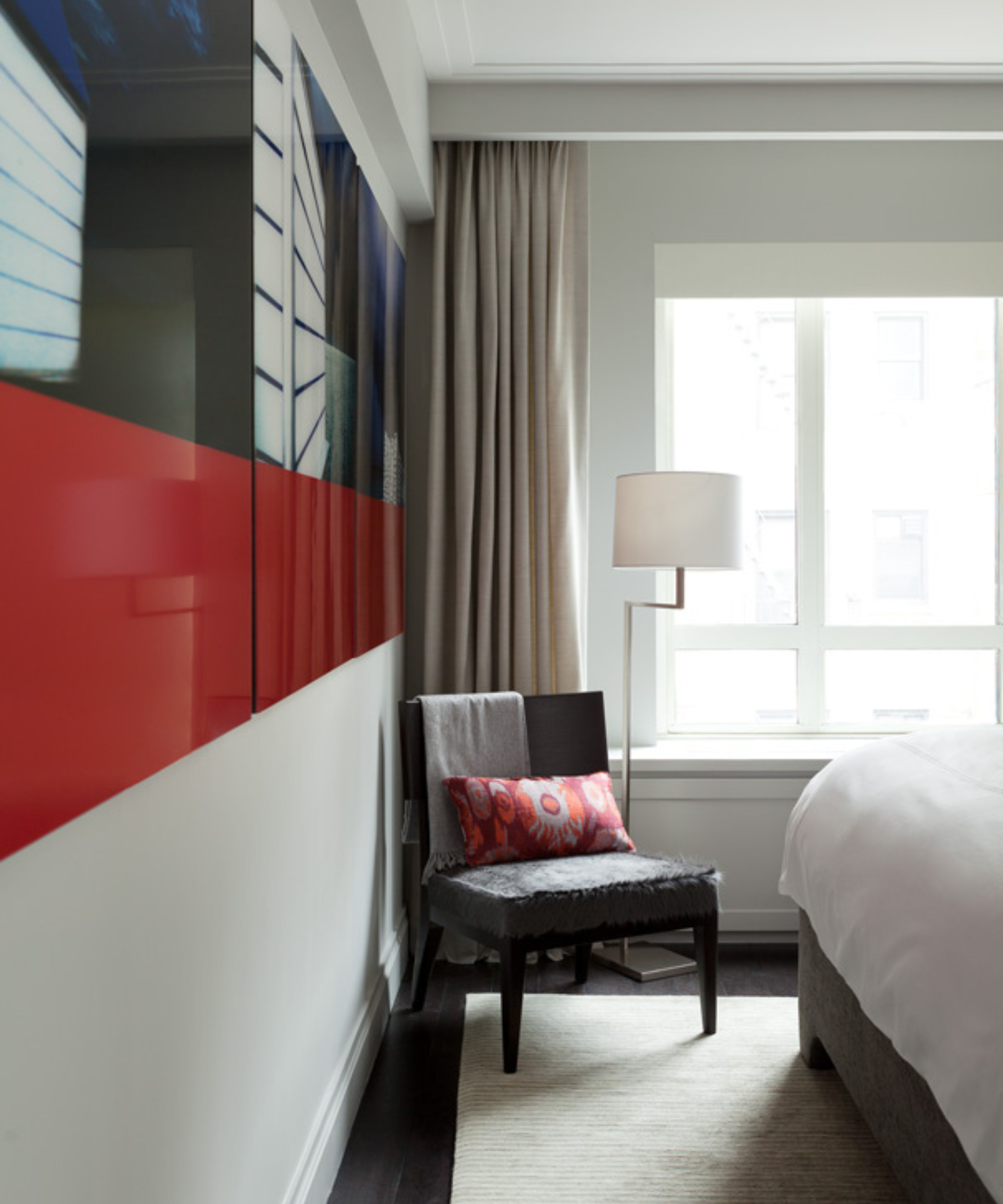 a corner in a bedroom with an accent chair with a pillow and a floor lamp in front of a window with curtains pushed to the side