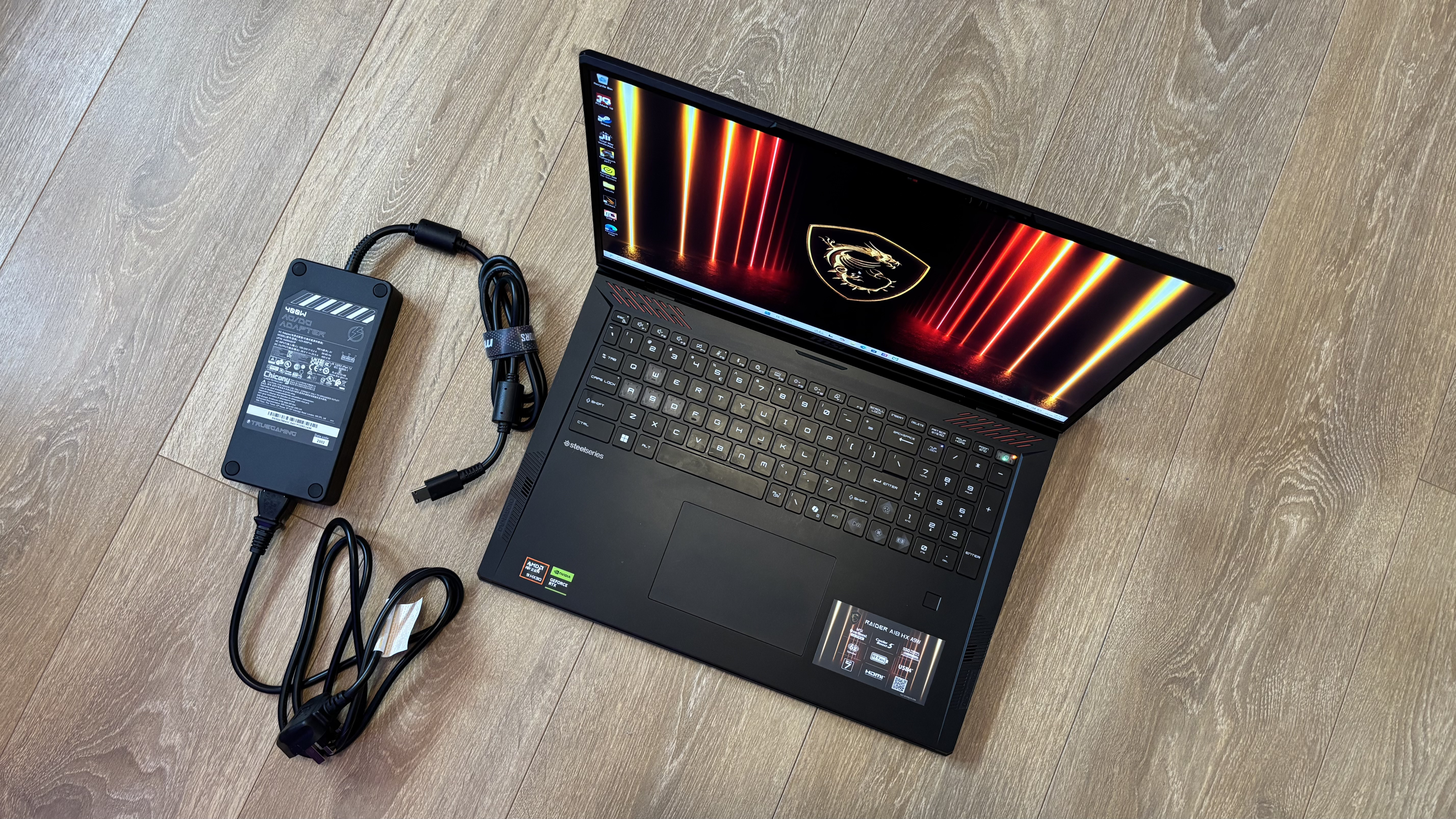 MSI Raider A18 HX with its charging cable on a wooden floor