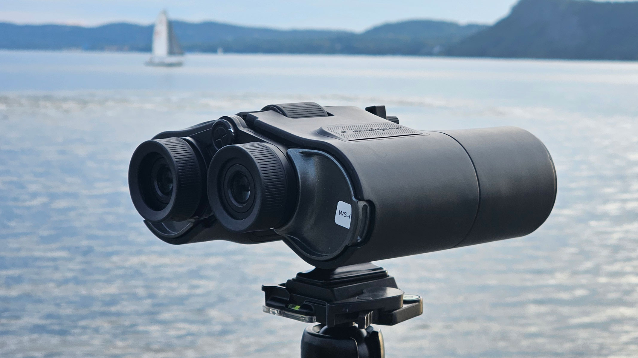 A side back view of the Unistellar Envision smart binoculars with water and a boat in the background.