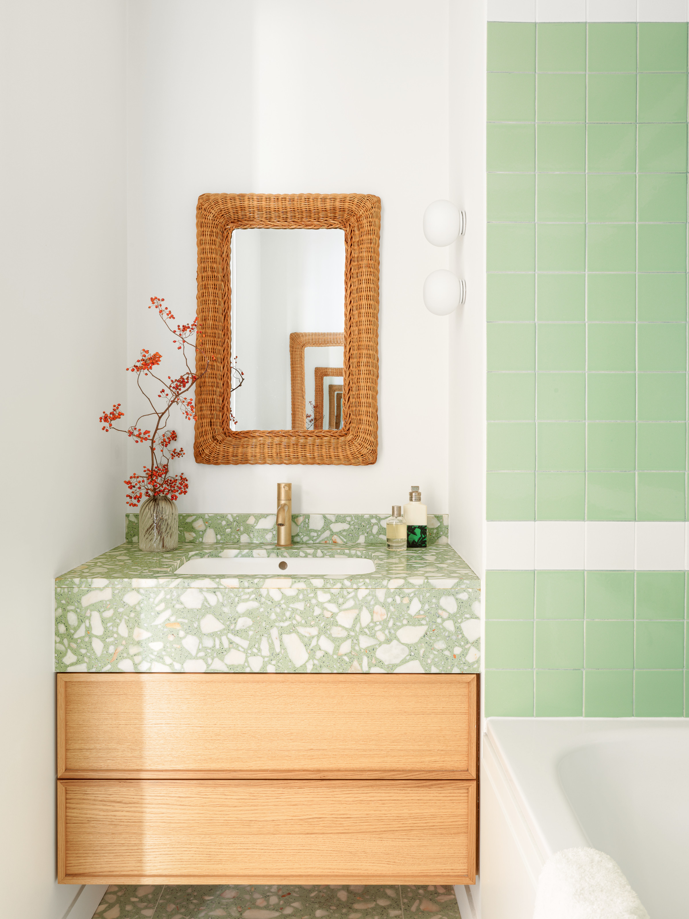 Bathroom with green and white tiles, oak vanity with green terrazzo worktop, and rattan mirror