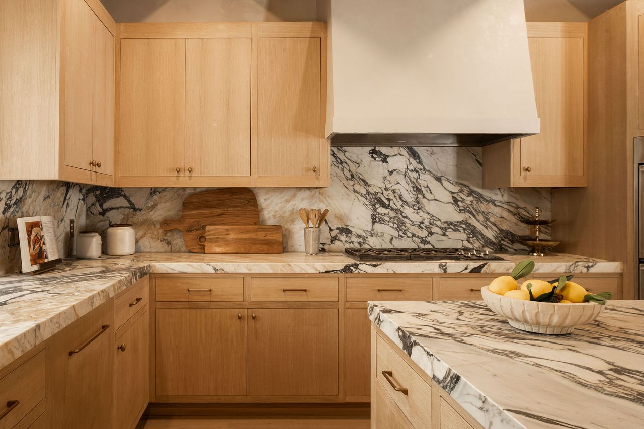 A kitchen with marble island top, backsplash and light wood cabinets