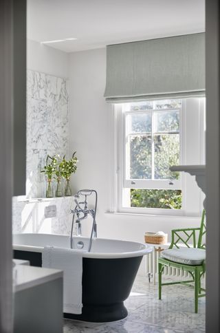 white bathroom with marble wall and floor, green chair, pale green blind, black painted roll top