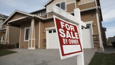 A red for sale sign hanging outside of a suburban two-story home.