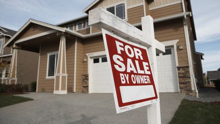 A red for sale sign hanging outside of a suburban two-story home.