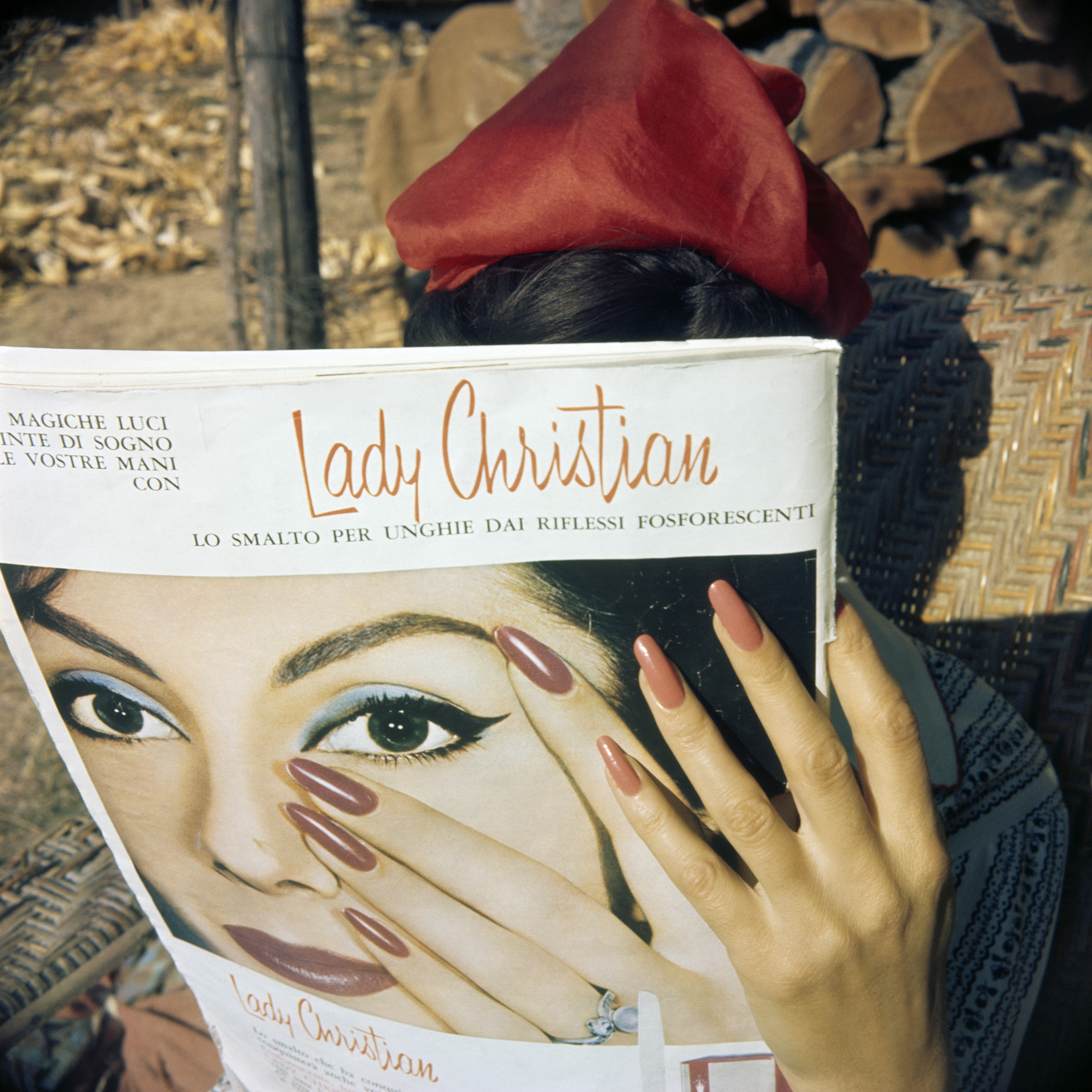 A woman in a red headscarf holds up an Italian nail varnish magazine advert, her painted nails echoing the model's pose on the page.