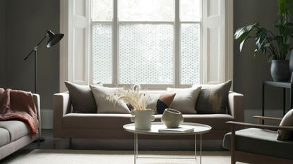 A living room with a grey couch against a large bay window covered in a patterned window film