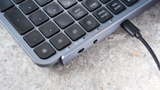 a black and grey budget wireless Bluetooth keyboard with a full-size layout and a numerical keypad is photographed against a blue background