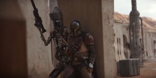 IG-11 and The Mandalorian take cover behind a wall.