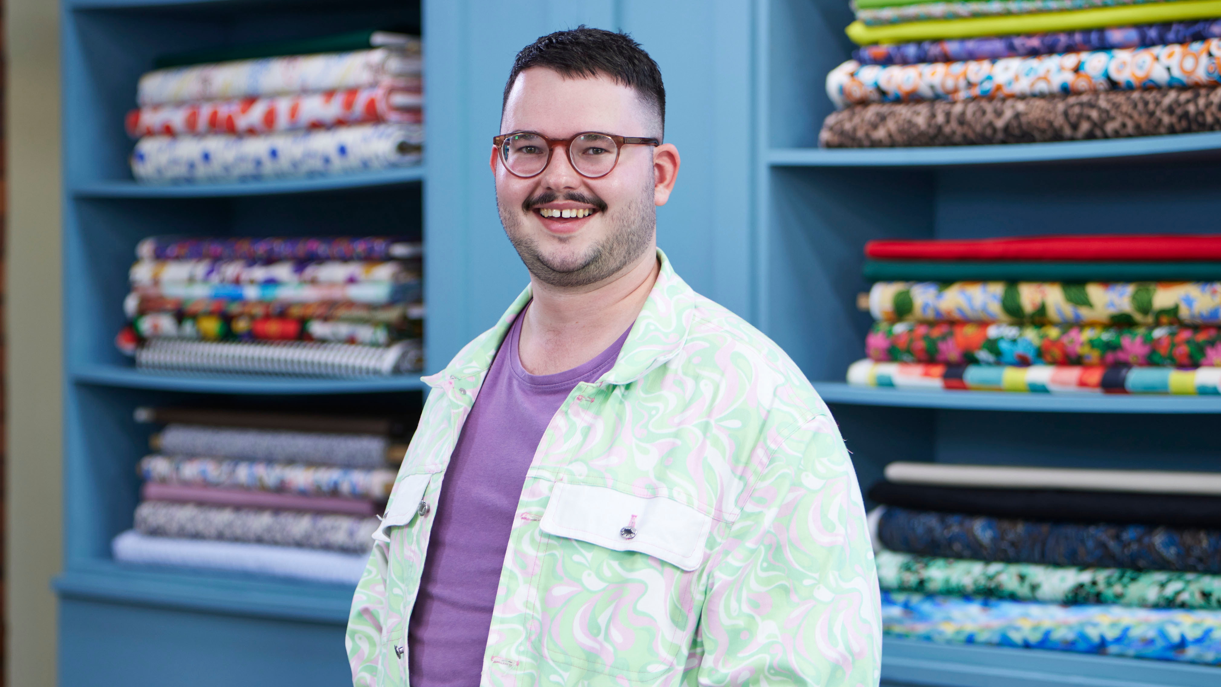 Kit standing in the Great British Sewing Bee studio and smiling for the camera