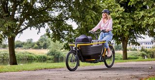 A women rides a black and yellow Raleigh Stride cargo bike in a park
