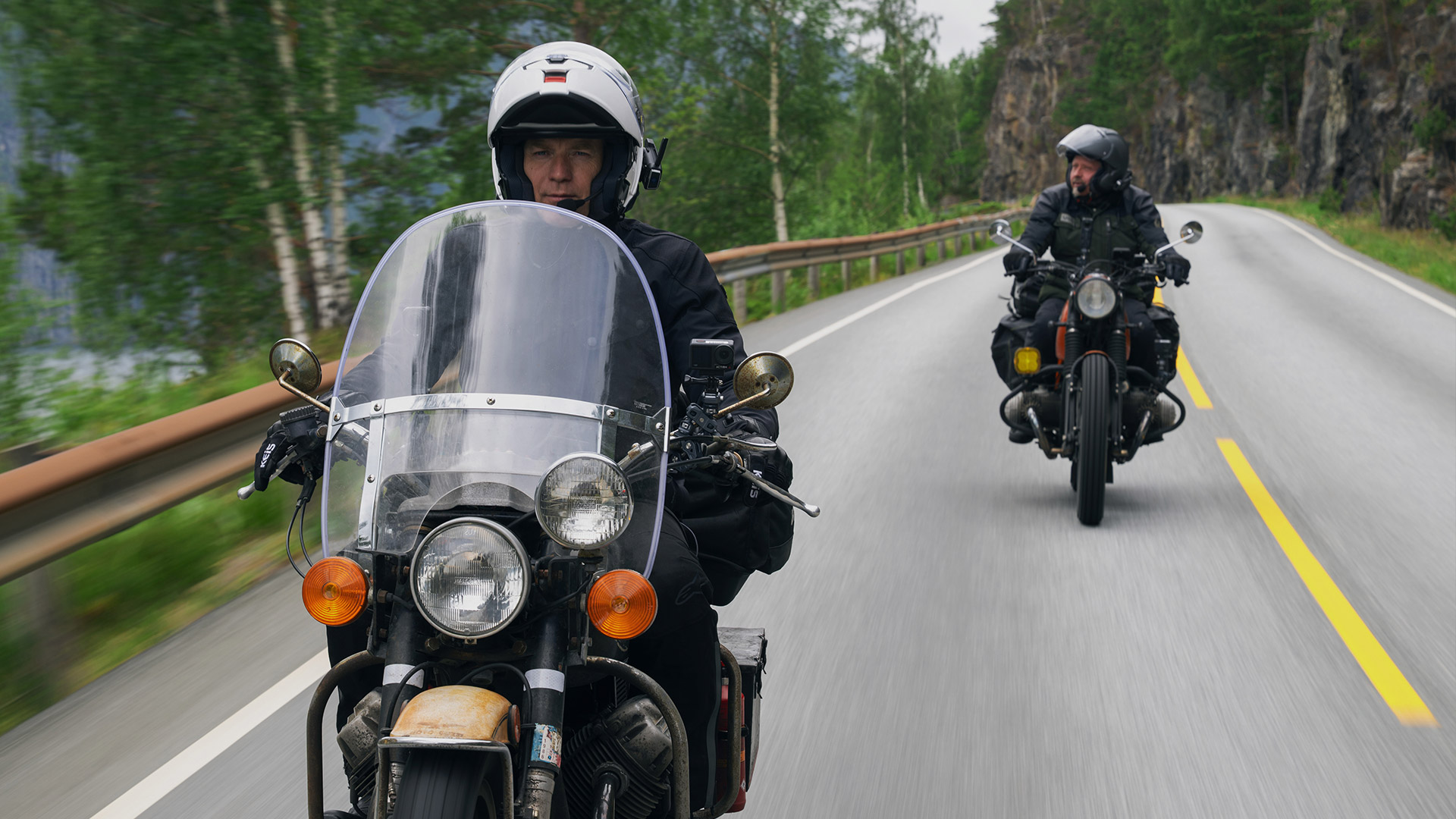 Two men riding bikes while on a road