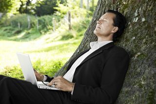 Businessman relaxing against a tree with his laptop