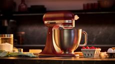 A red KitchenAid Artisan Plus Stand Mixer on a kitchen counter surrounded by baking ingredients. 