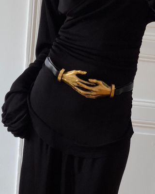 A woman wearing a black dress with Khaite's brass hand belt.