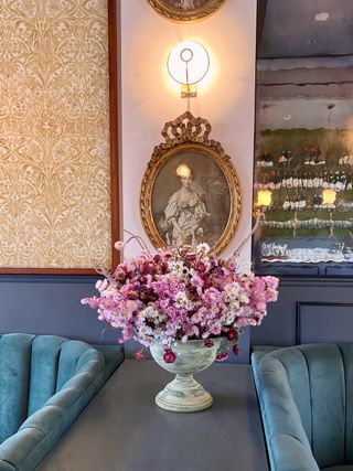 large urn with pink dried flowers in living room, wallpaper, two turquoise couches, vintage painting