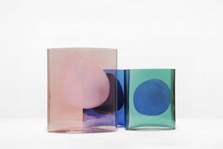 Cynlinder glass vases in pink, blue and green featuring a circular form in the middle photographed against a white background
