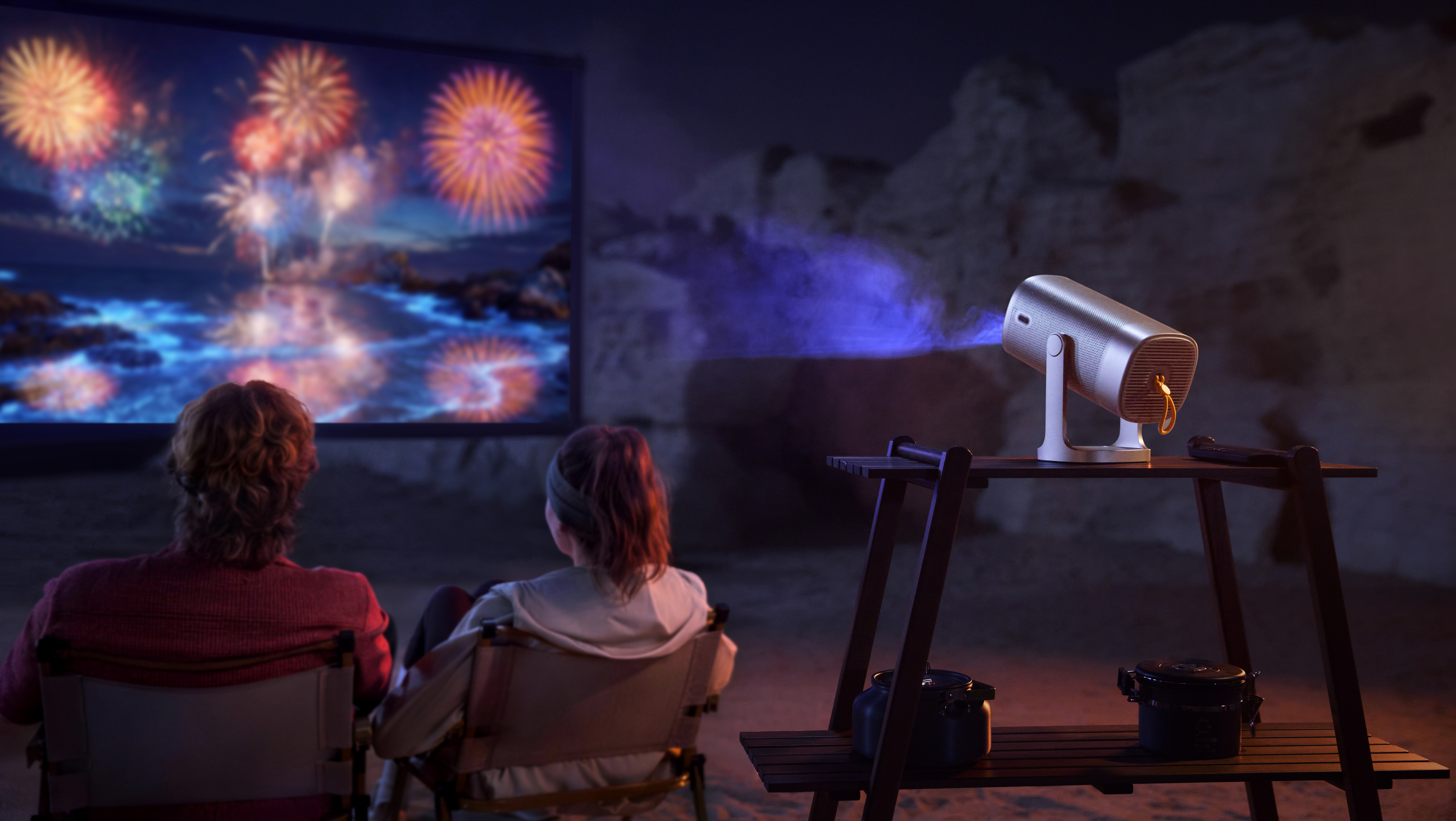 A couple watching a movie outdoors with a projector set up behind them.