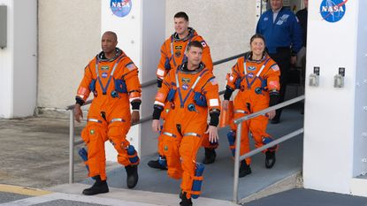The four Artemis II astronauts walking down a ramp in their orange flightsuits