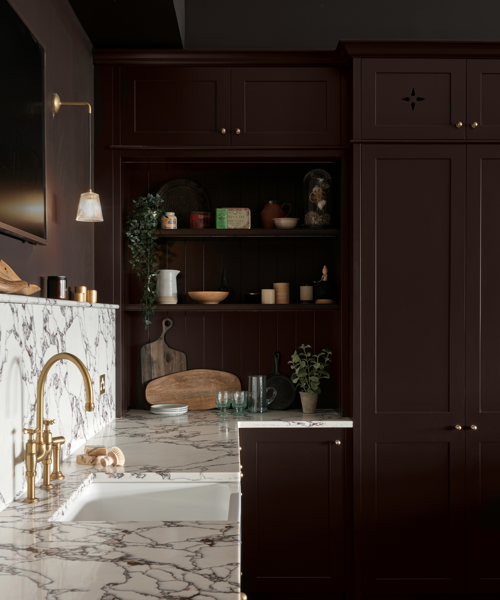 A moody kitchen with brown full length shaker cabinetry paired with paler pink perimeter cabinets and marble countertops
