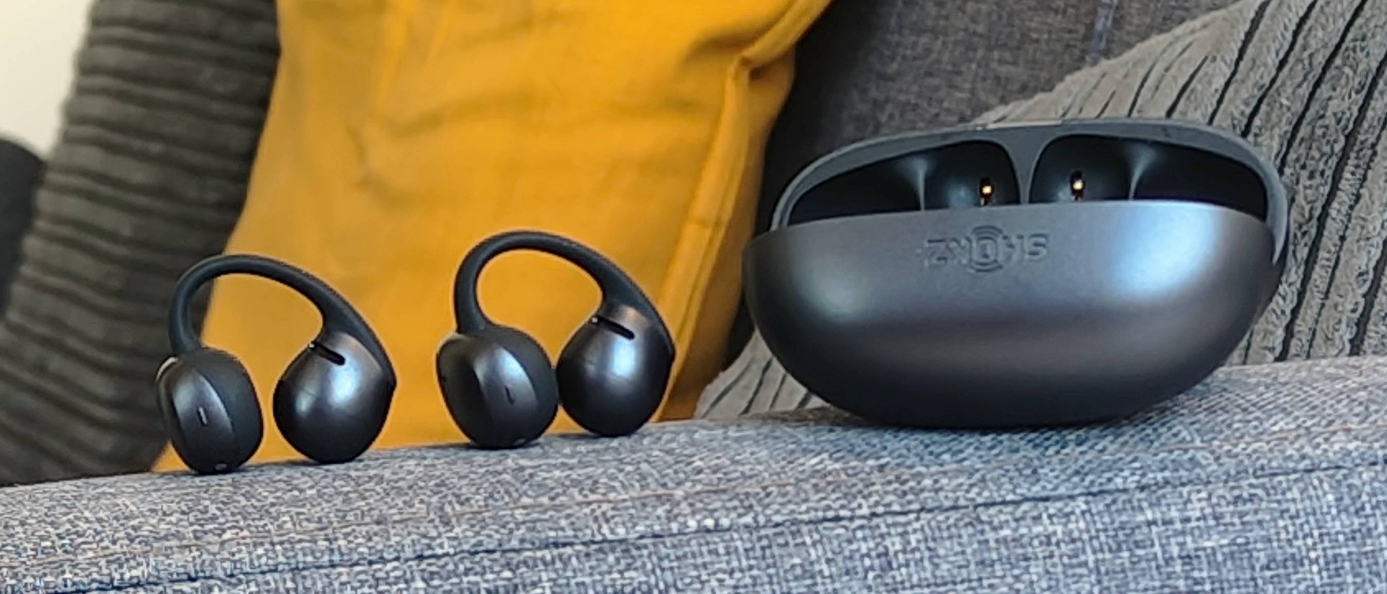 The Shokz OpenDots Air case and earbuds on the arm of a sofa.