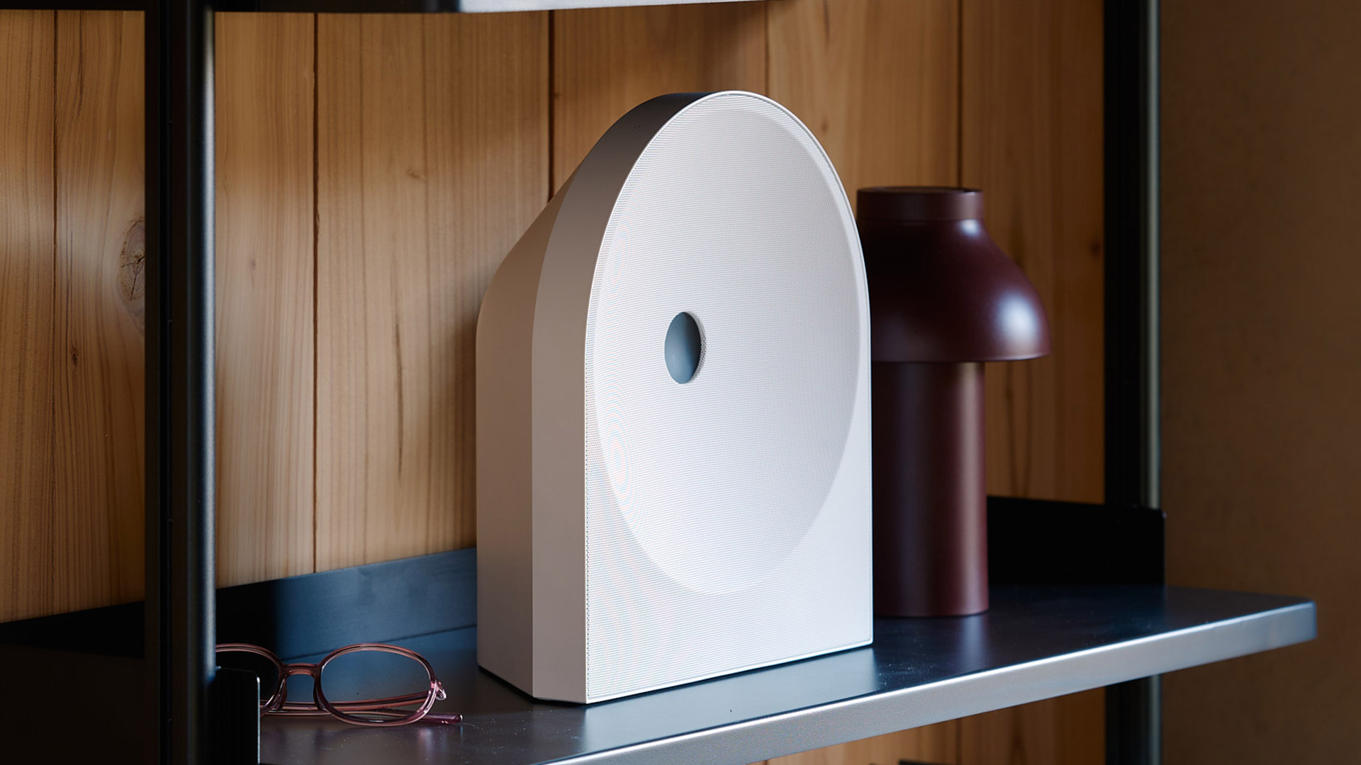 Samsung Music Studio 5 smart speaker in white, on a shelf with a wood panel behind it