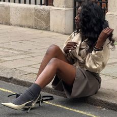 @_livmadeline wears a cropped trench coat, grey Bermuda shorts, grey socks and white slingback heels