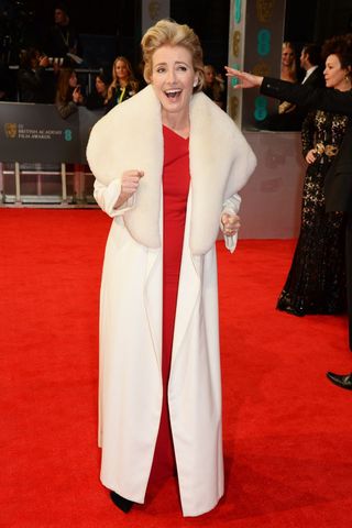 Emma Thompson wearing a red gown and white fur collar coat