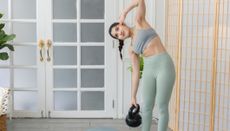 Woman in sportswear, holding a kettlebell in one hand and leaning to the side from the waist