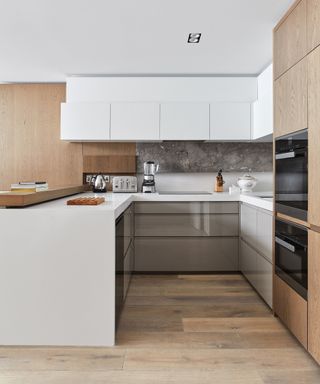 An example of small kitchen storage ideas showing a u-shaped kitchen with flat white cabinets and two built-in ovens