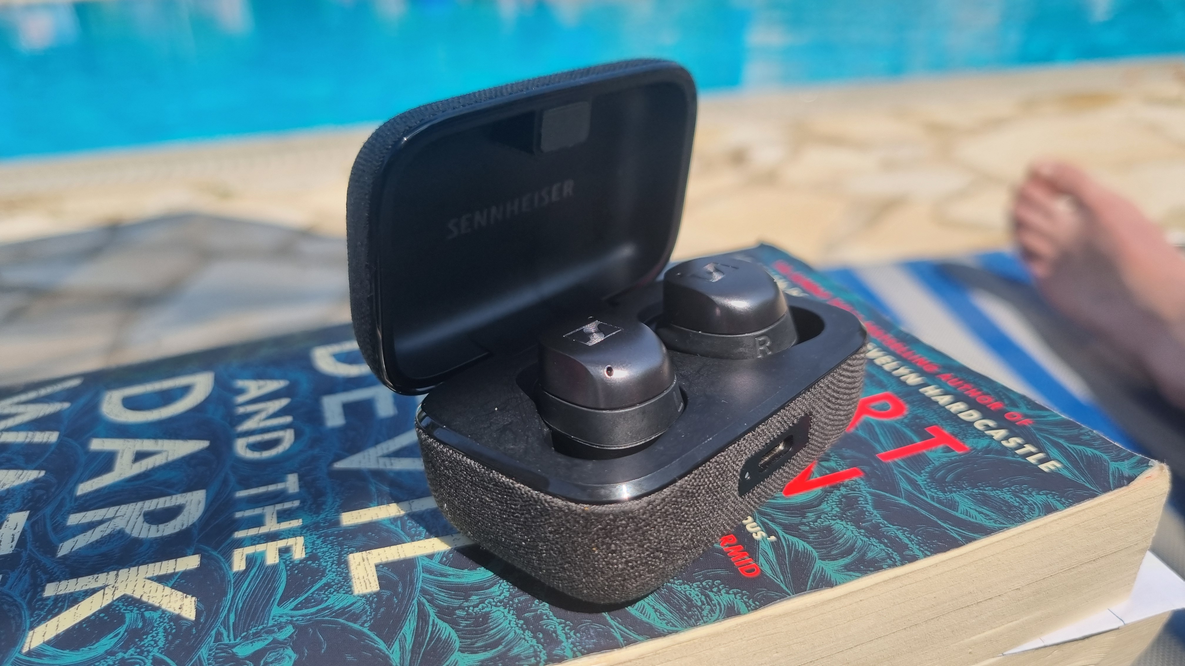 Sennheiser Momentum True Wireless 4 earbuds in a case by the pool, with bonus foot pic