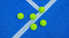 Five pickleball balls next to a blue court line