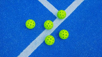 Five pickleball balls next to a blue court line