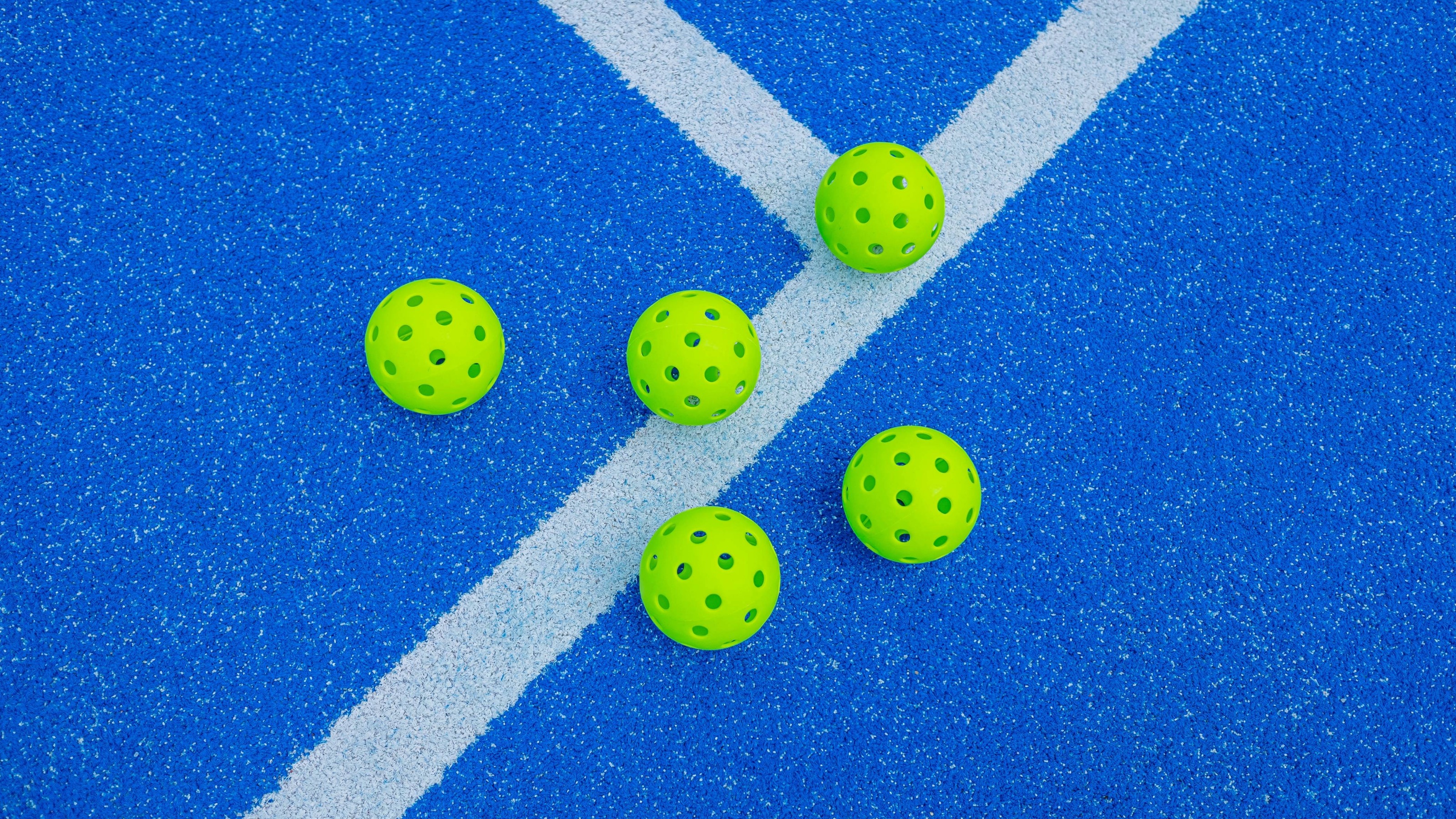 Five pickleball balls next to a blue court line