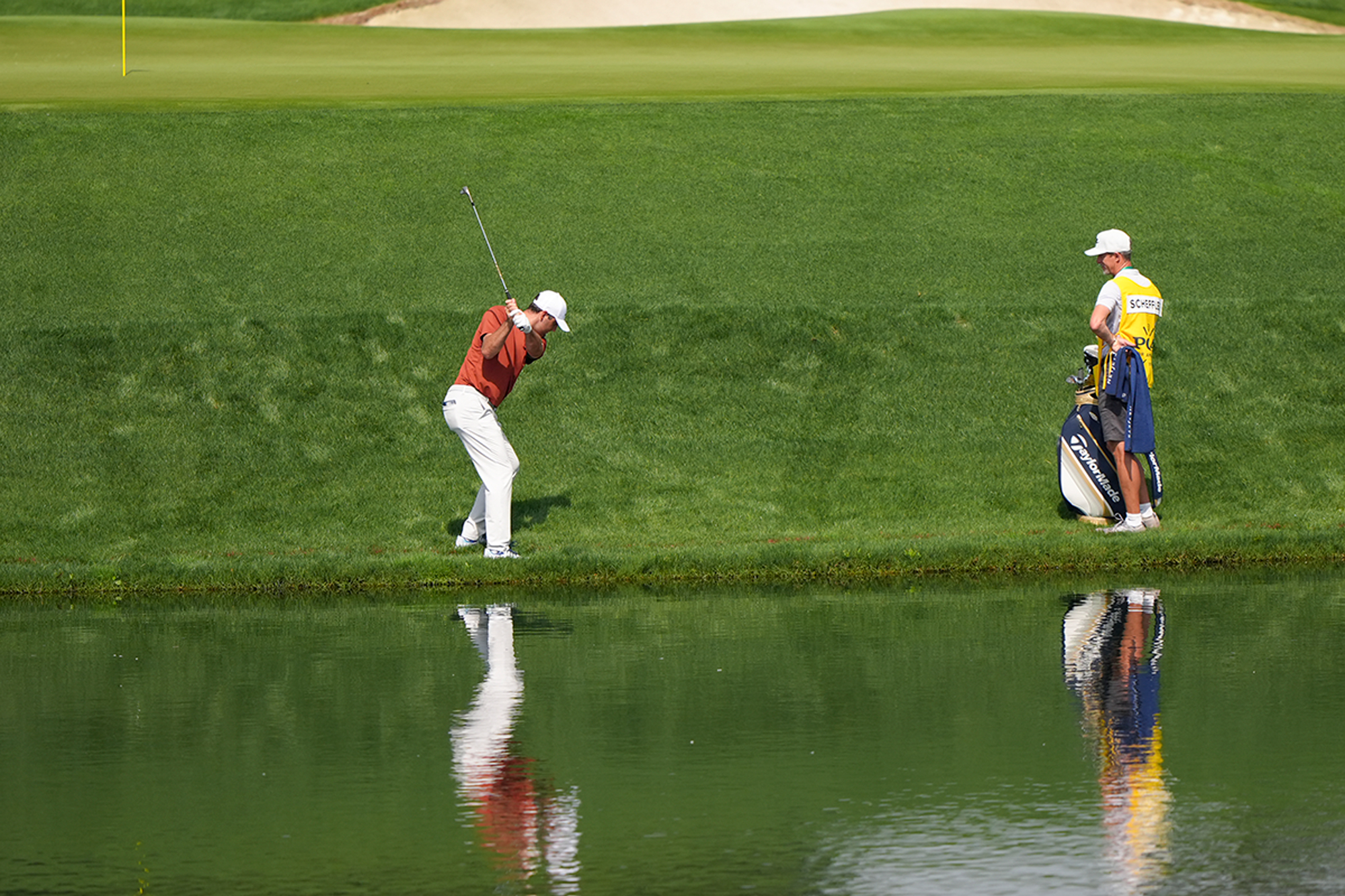 Scottie Scheffler hitting a shot from just over the water near the green at Quail Hollow during the PGA Championship